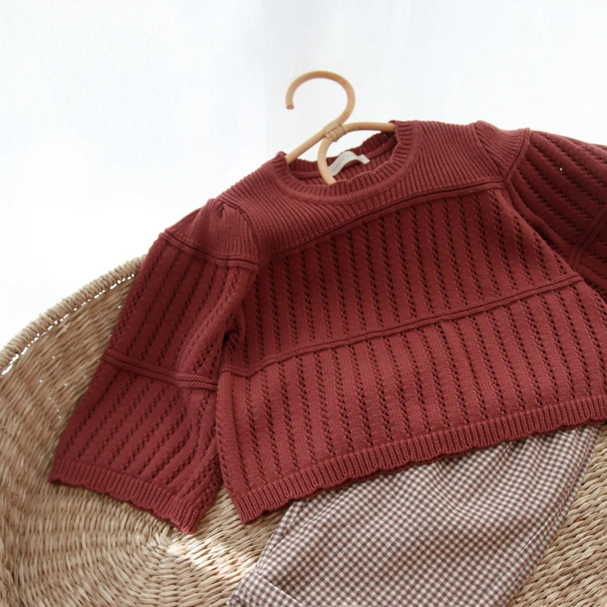 Red sweater and plaid pants on a wooden hanger over a woven surface