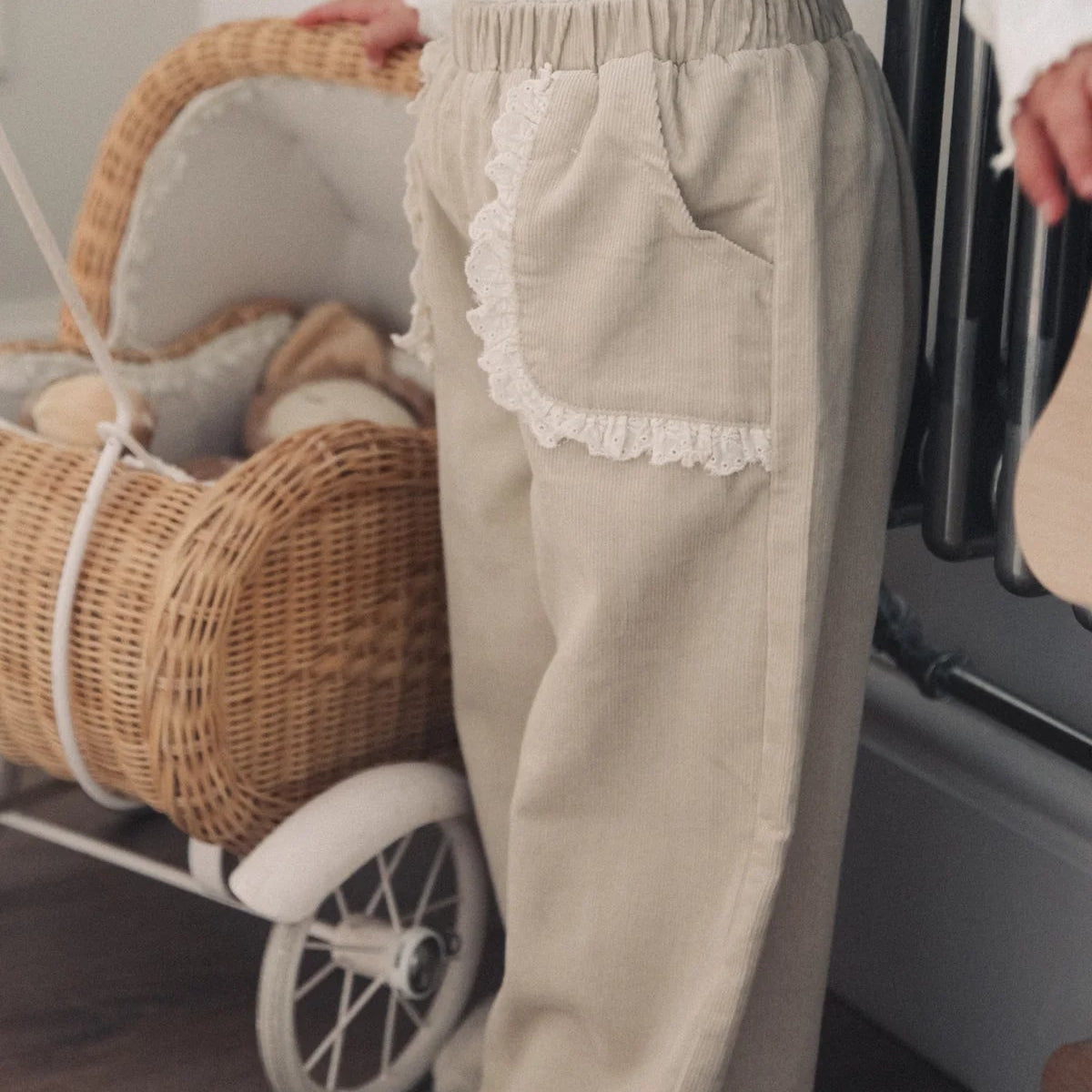 Person wearing beige pants with lace trim holding a wicker baby buggy.