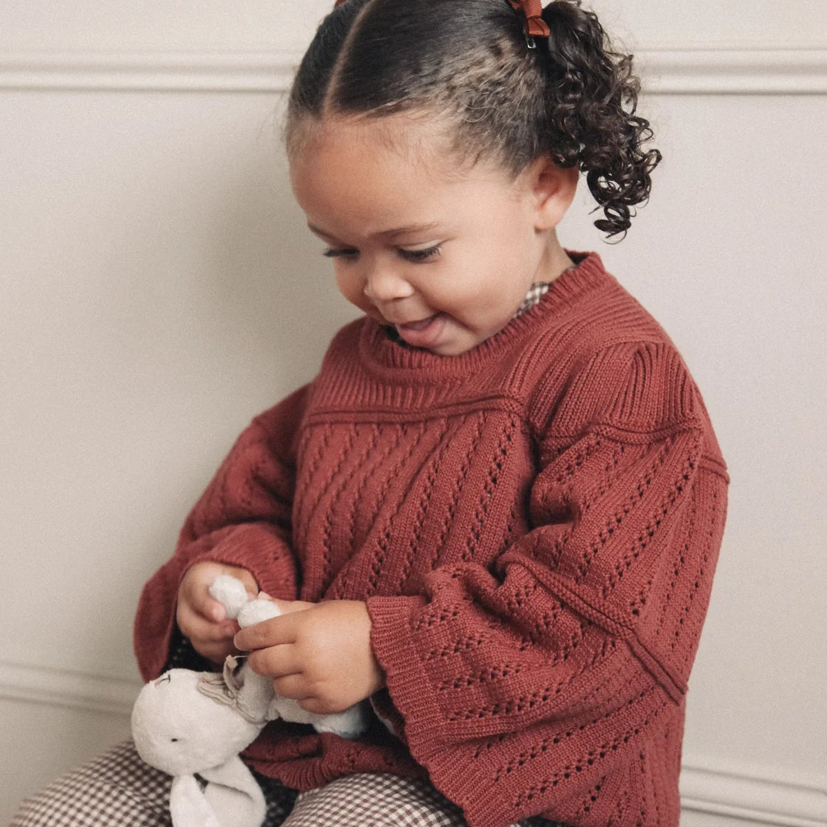 Child wearing a red sweater sitting on a stool with a white background