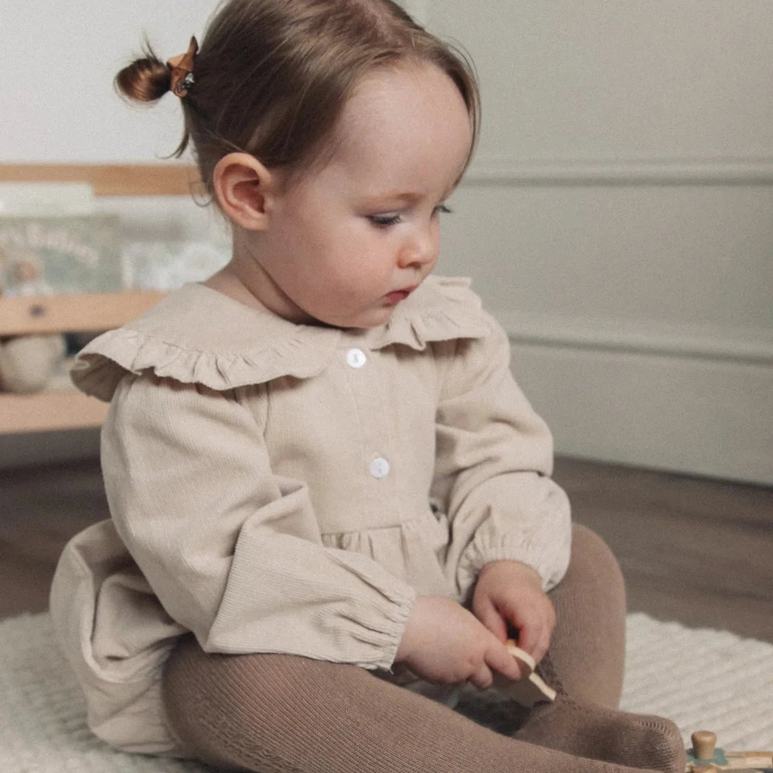 Child in a beige dress sitting on the floor with toys around