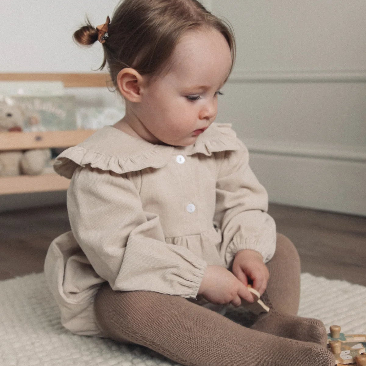 Child in a beige dress sitting on the floor with toys around