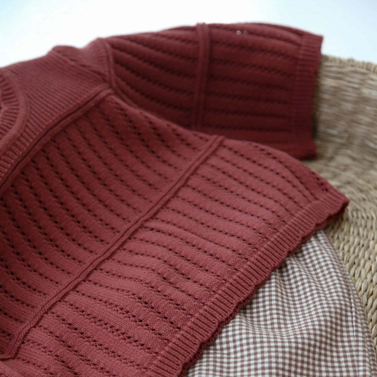 Red ribbed sweater and checkered fabric on a woven surface